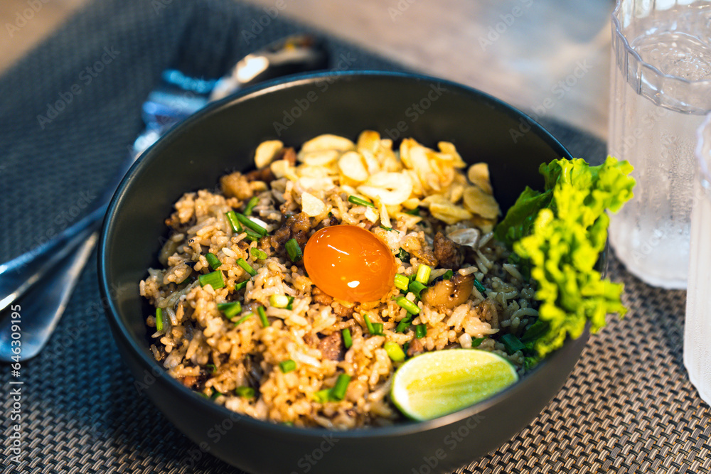Beef fried rice with egg yolk on top in a black bowl on a restaurant table. Beef fried rice with egg yolk on top in a black bowl on a restaurant table.