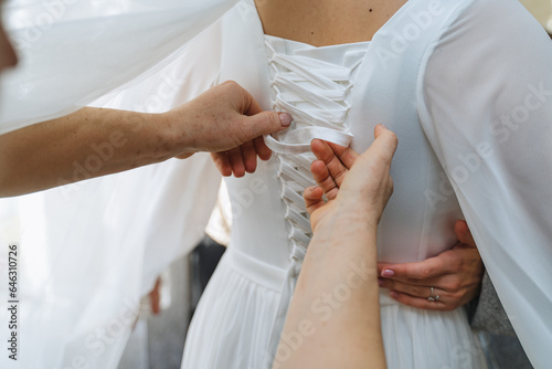Elegant bride asking mother to tighten corset on wedding dress