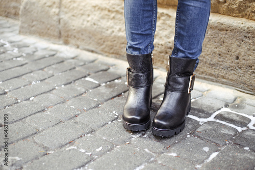 Women's legs in blue jeans and black leather winter boots. Stylish winter footwear