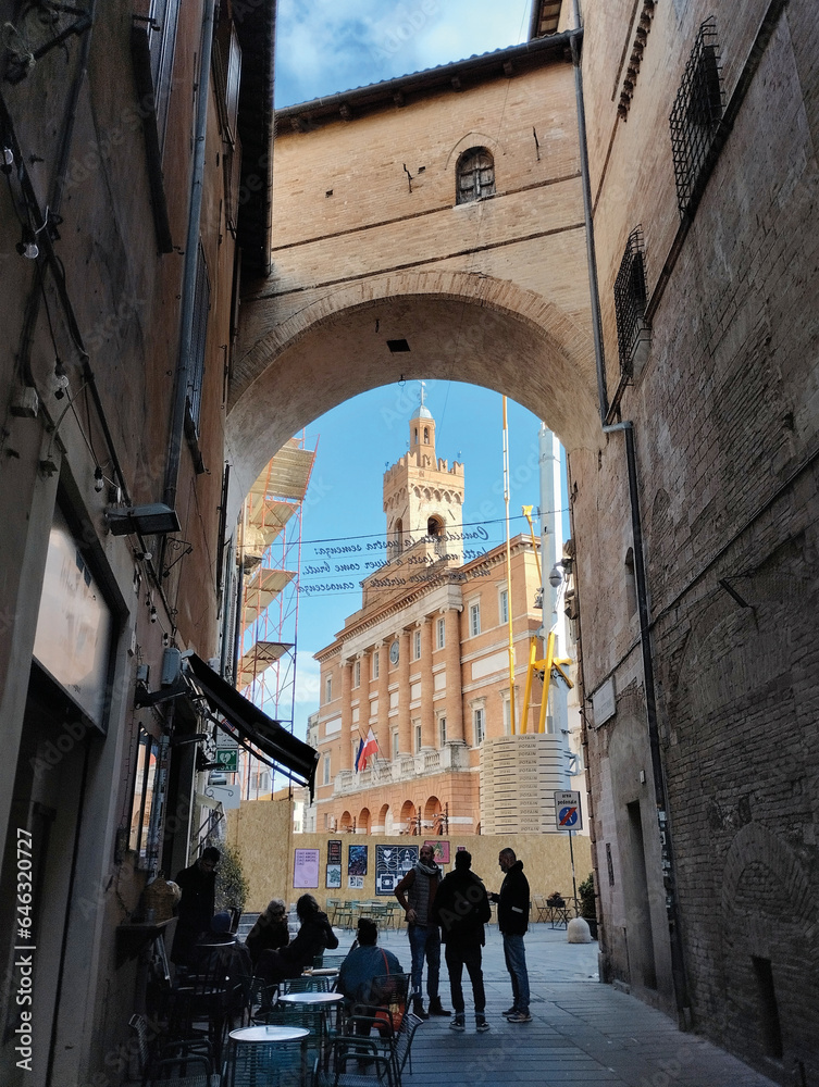 A delightful view of lively Piazza della Repubblica in Foligno, captured from an archway, with silhouettes of people enjoying their time.