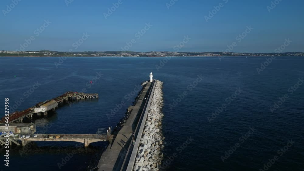 Brixham, Torbay, South Devon, England: DRONE VIEW: Brixham Harbour Lighthouse; Outer Harbour Wall and a Yacht heading out to Sea. Brixham is a popular UK holiday resort. Brixham, Torbay, South Devon, England: DRONE VIEW: Brixham Harbour Lighthouse; Outer Harbour Wall and a Yacht heading out to Sea. Brixham is a popular UK holiday resort.