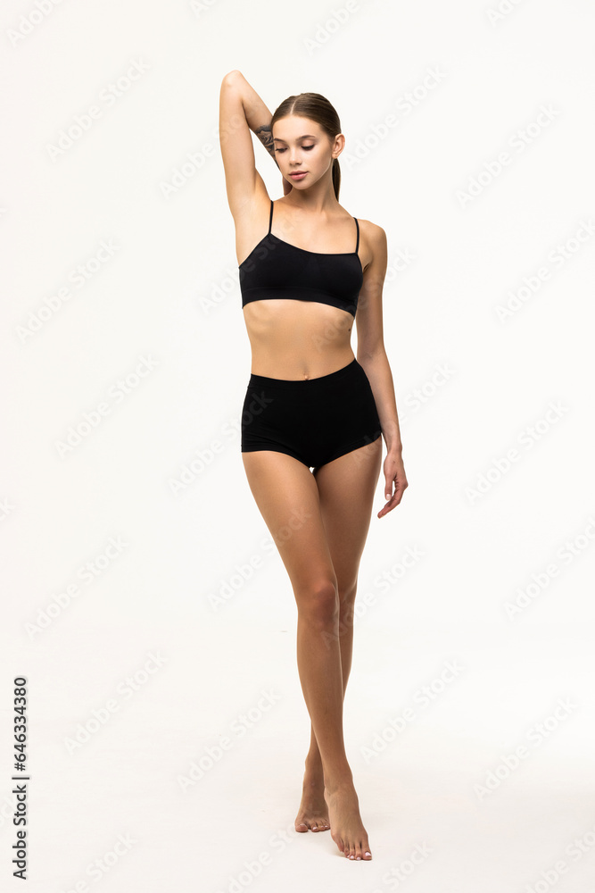 Full-length portrait of young slim woman posing in black underwear isolated over grey background.