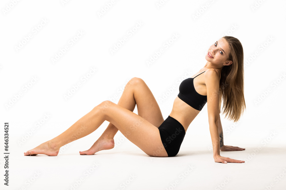 Young woman with perfect body in black underwear sitting on floor on white background