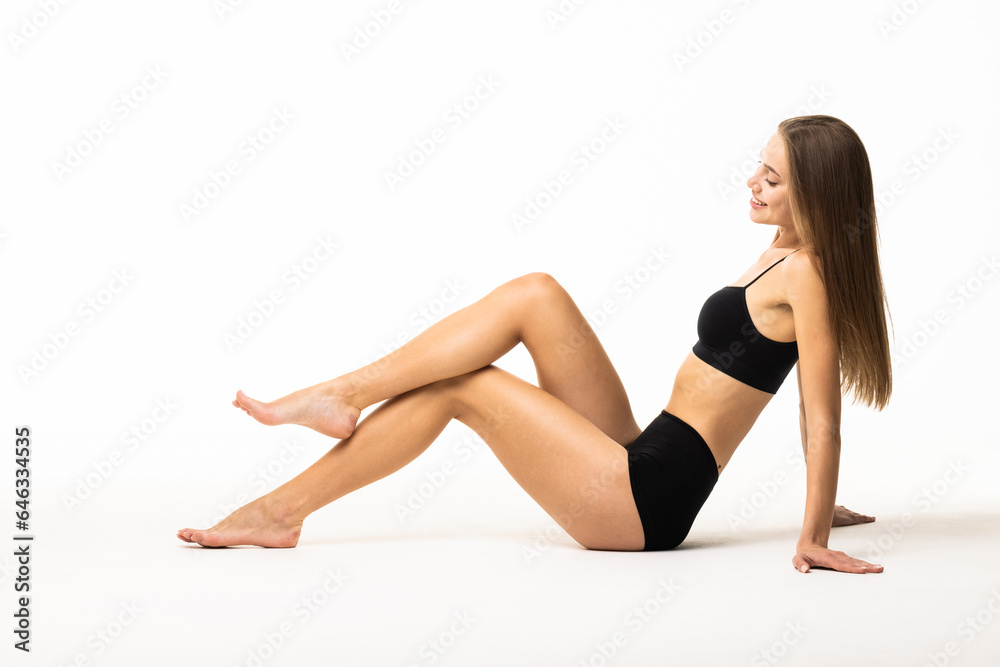 Portrait of young woman sitting on floor, posing in black underwear isolated over white background.