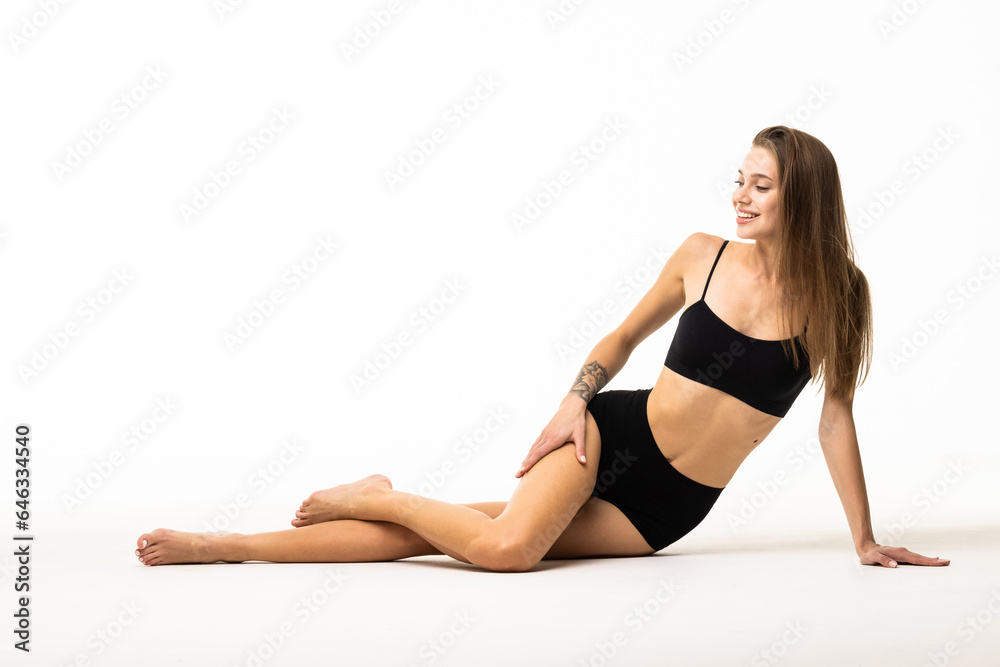 Portrait of young woman sitting on floor, posing in black underwear isolated over white background.