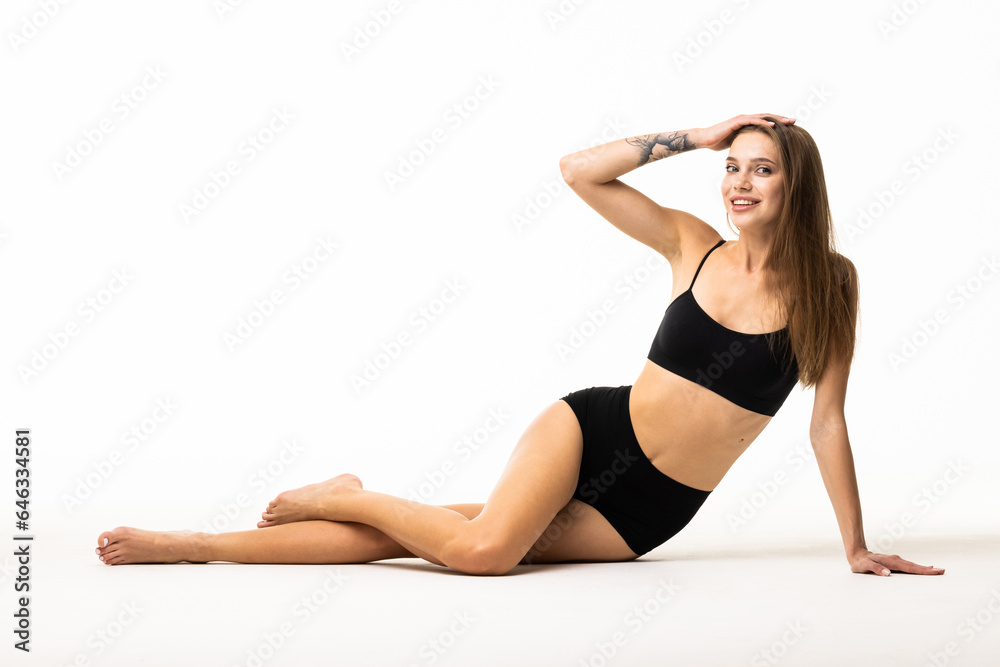 Portrait of woman sitting on floor, posing in black underwear isolated over white background.