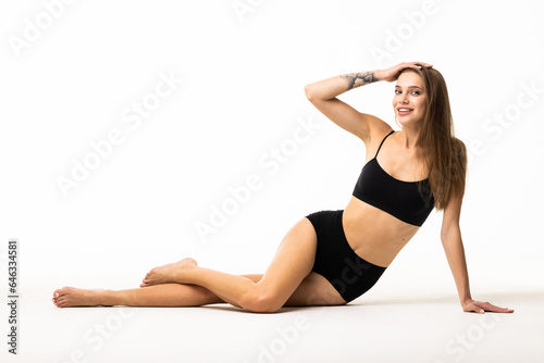 Portrait of woman sitting on floor, posing in black underwear isolated over white background.
