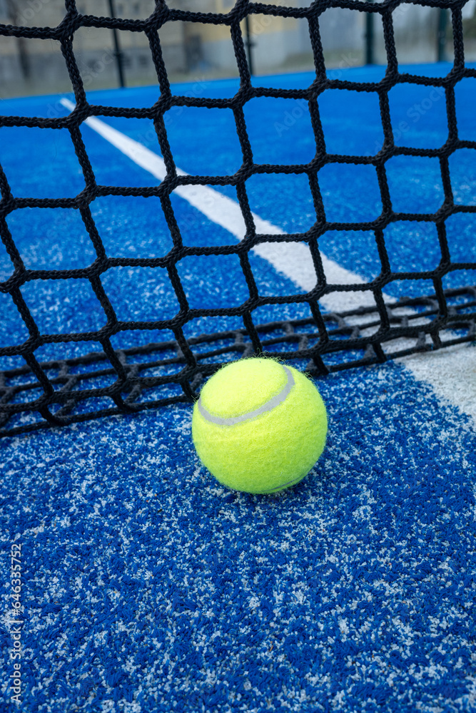 Yellow ball on floor in front of paddle net in blue court outdoors. Padel tennis