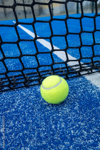 Yellow ball on floor in front of paddle net in blue court outdoors. Padel tennis © Vic