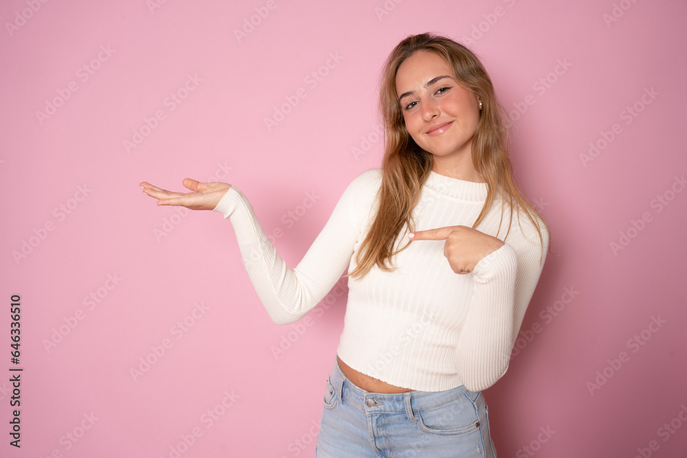 Excited young woman holding palm open for new product or sale presentation. Overjoyed happy blond girl with open mouth point finger at arm with copy space for promotion isolated over pink studio wall Excited young woman holding palm open for new product or sale presentation. Overjoyed happy blond girl with open mouth point finger at arm with copy space for promotion isolated over pink studio wall
