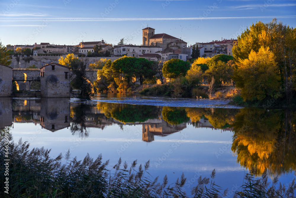 View of the city of Zamora and watermills and the San Pedro Church in the background in autmn at sunset reflected in the Duero river. Spain - obrazy, fototapety, plakaty 