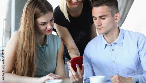 A group of people in a cafe communicate with a cup of coffee looking at the smartphone app and photos from the vacation