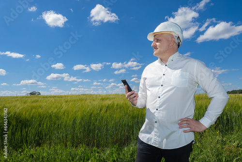 Architect stands in field. Man builder in hardhat. Businessman thought about building farm. Architect chooses place for building. Man with phone in countryside. Builder agricultural company in field