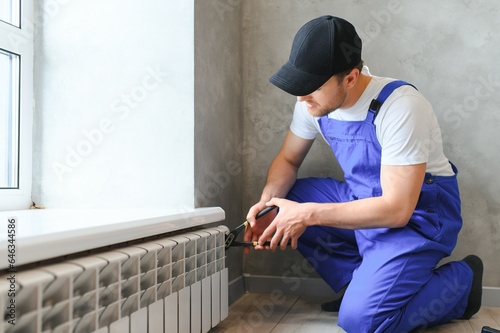 young man plumber checking radiator while installing heating system in apartment