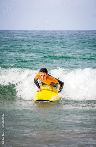Surfer With Straight Face In Concentration Trying Hard To Get On The Board To Catch A Wave In The Foam. Vertical Photo