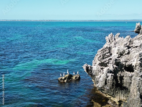 Rocks far from the coast in the ocean with birds sitting on top on a clear sunny day with beautiful clear blue water