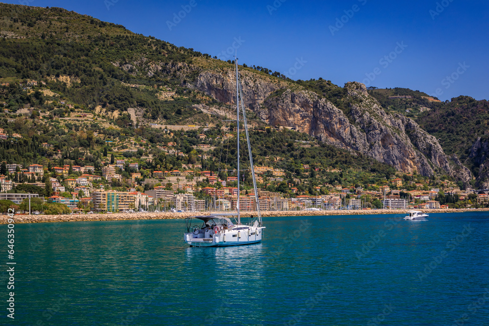 Mediterranean Sea and coastline with a beach and a boat in the water in Menton on the French Riviera, South of France on a sunny day, panoramic view
