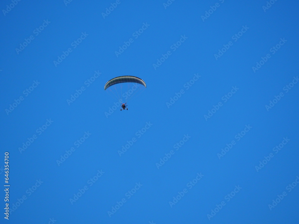 vista frontal de parapente con vela fija color blanco y negro y motor de hélice volando bajo el cielo azul sobre las montañas del montsec aragones, huesca, españa, europa vista frontal de parapente con vela fija color blanco y negro y motor de hélice volando bajo el cielo azul sobre las montañas del montsec aragones, huesca, españa, europa