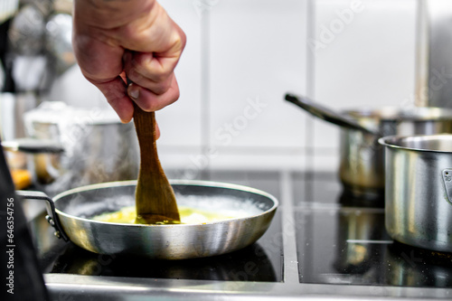 man chef cooking tasty scrambled eggs in frying pan on kitchen