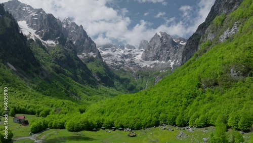 Green valley with a meadow and stunning mountains with snow, aerial view. Clouds over the mountain peak. Establishing view, crane shot.