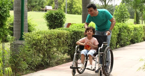 Stock video of father walking with disabled son in wheelchair at park
