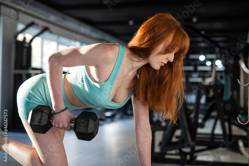 red-hair female trainer holding dumbbells during an exercise class at the gym