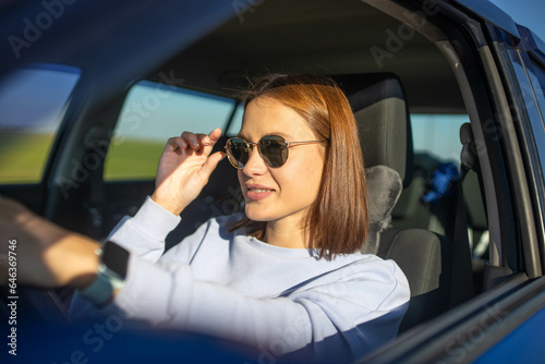 Beautiful young woman driver driving a car on a sunny day smiling.