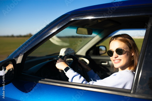 Beautiful young woman driver driving a car on a sunny day smiling.