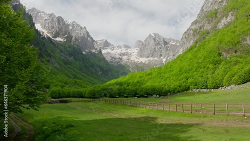 opening shot grebaje valley in montenegro, aerial view. green meadow and sharp mountain summit, look like alpine scenery. fly low over the meadow and wooden fence photo