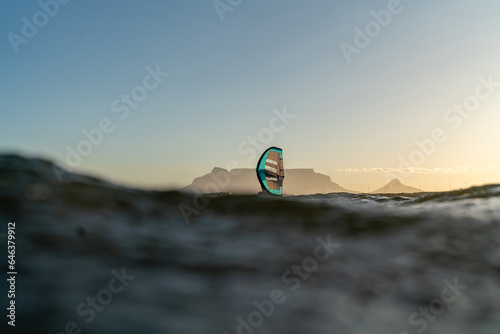 A man is wing foiling in-front of Table Mountain using handheld inflatable wings and hydrofoil surfboards in a blue ocean, rider on a wind wing board. Cape Town South Africa Sunset selective focus.
