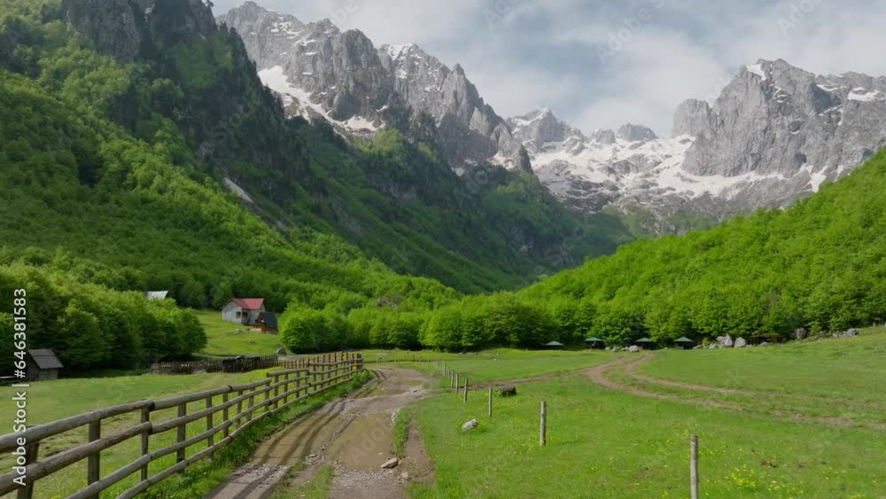 wooden fence and dirt road in mountain valley in spring, countryside village. aerial view fly low over the road. sunny summer day. green landscape around.
