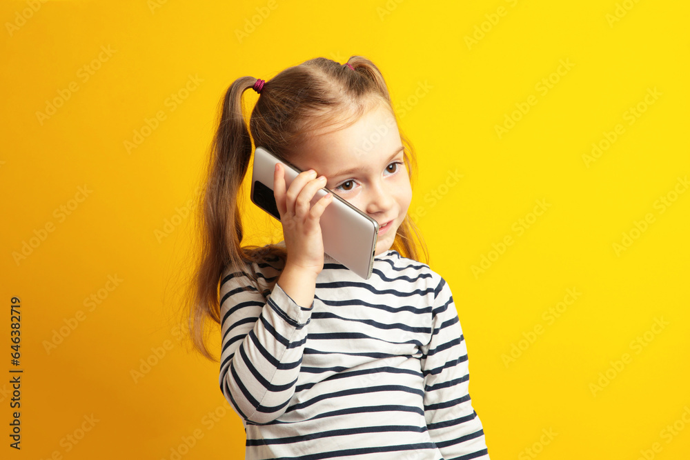 Funny little girl talking on mobile phone on yellow background. Funny little girl talking on mobile phone on yellow background.
