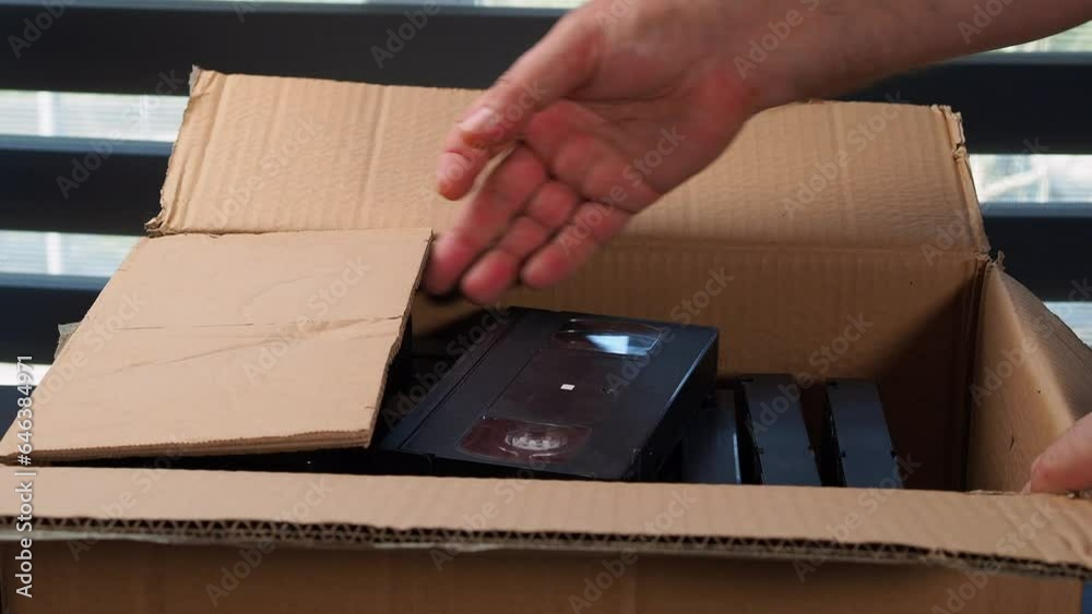 Old VHS tapes in a cardboard box. A man opens a cardboard box with VHS