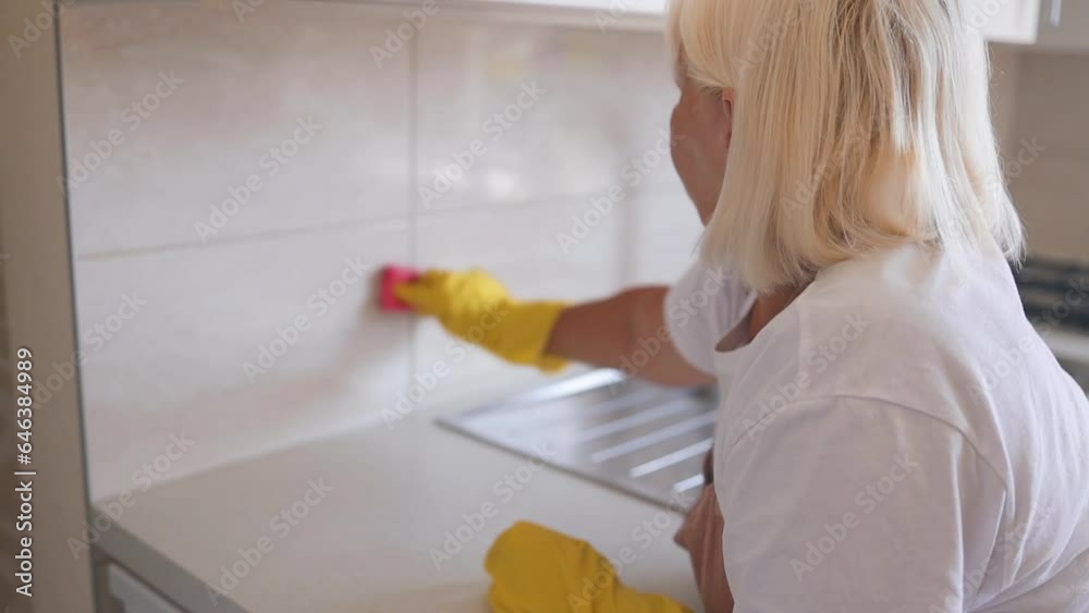 Housewife 50s woman housekeeping on weekend.Woman in yellow protective rubber gloves cleaning kitchen cabinets with sponge. High quality FullHD footage Housewife 50s woman housekeeping on weekend.Woman in yellow protective rubber gloves cleaning kitchen cabinets with sponge. High quality FullHD footage