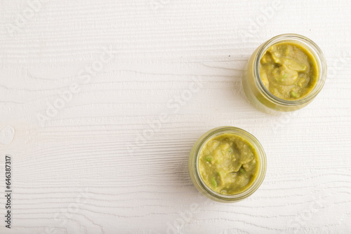 Baby puree with vegetable mix, broccoli, avocado in glass jar on white wooden, top view, copy space