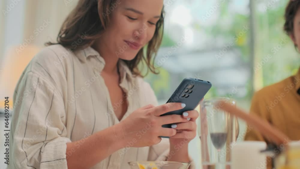 Medium close up of young concentrated woman typing message on smartphone while sitting at dinner table with glass of wine at home Medium close up of young concentrated woman typing message on smartphone while sitting at dinner table with glass of wine at home