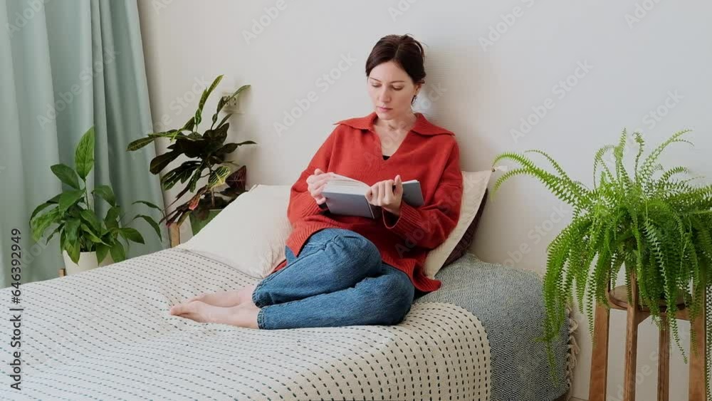 Woman relax sit on sofa with cat reading a book. Attractive woman in a orange sweater sitting on the couch and reading a book at home surrounded by green plants. Woman relax sit on sofa with cat reading a book. Attractive woman in a orange sweater sitting on the couch and reading a book at home surrounded by green plants.