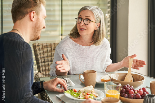 Positive senior mother in glasses communicating with son at kitchen