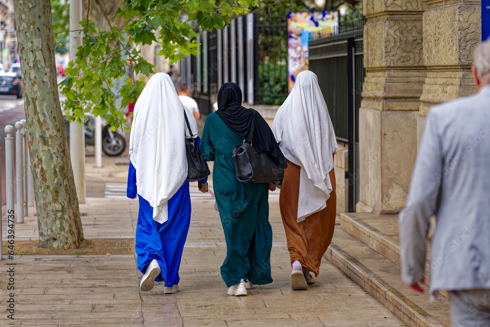 Rear view of three young muslim women at French City of Toulon on a cloudy late spring day . Photo taken June 9th, 2023, Toulon, France.