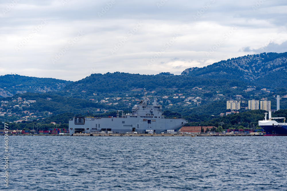 Moored warships with helicopter carrier Dixmude L-9015 at French Navy Naval Base at City of Toulon on a cloudy late spring day. Photo taken June 9th, 2023, Toulon, France.