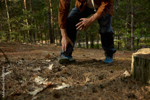 Senior man sprained leg during hiking trip outdoors in forest