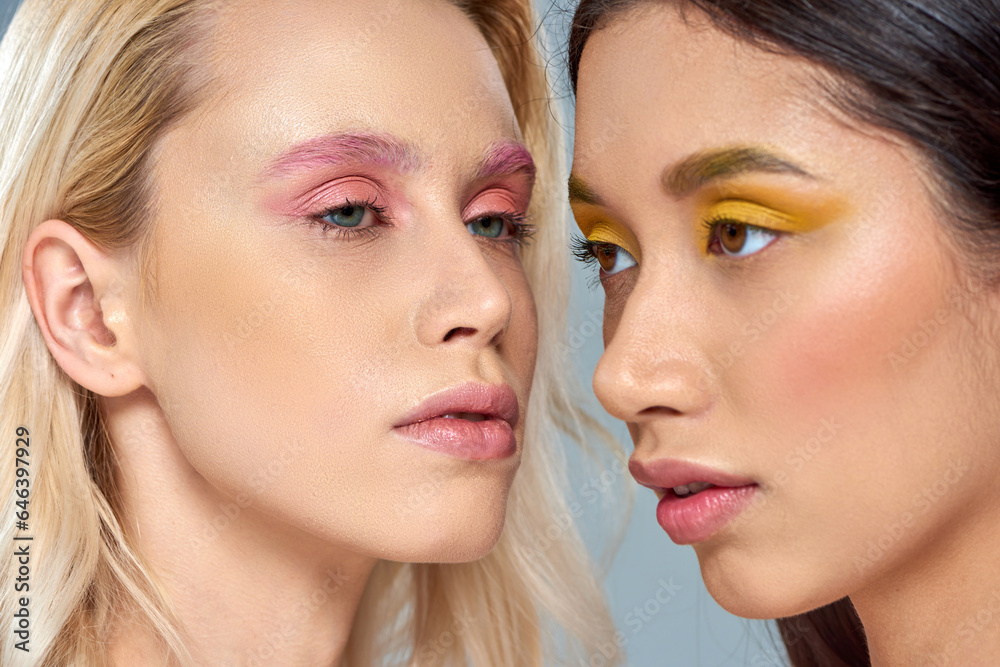 diverse beauty concept, multiethnic women with vibrant eye makeup posing together on blue backdrop diverse beauty concept, multiethnic women with vibrant eye makeup posing together on blue backdrop