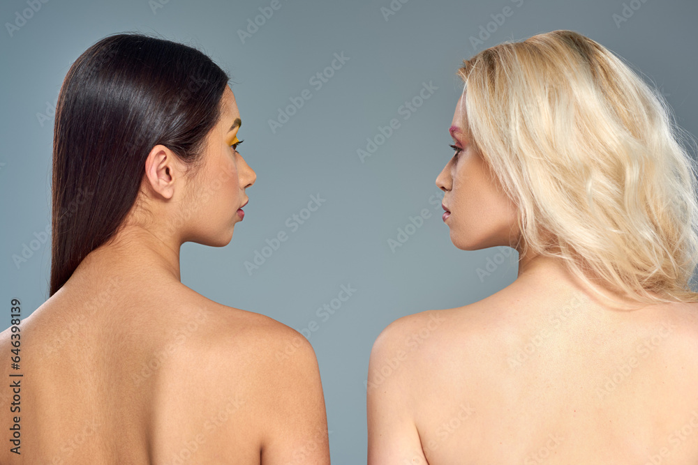 multiethnic models with bare shoulders looking at each other on blue backdrop, diverse beauty multiethnic models with bare shoulders looking at each other on blue backdrop, diverse beauty