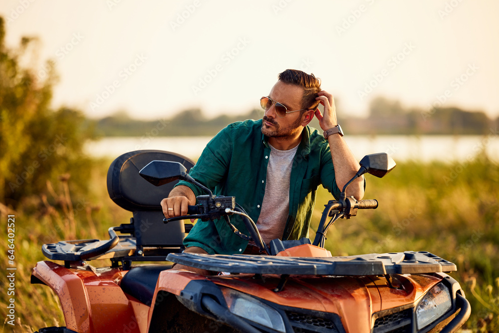 Fototapeta premium An adult man with sunglasses on, sitting on a quad bike and looking around.