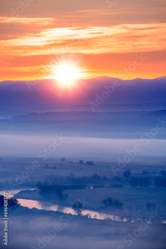 Aerial view of the sunrise over the valley in beautiful early morning mist in the highlands. Low clouds and fog cover the sleeping meadow. Hills valley mists landscape. Serene moment in rural area