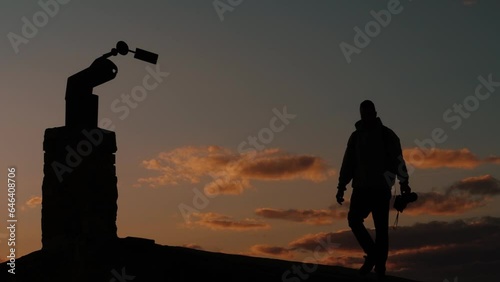 Silhouette of a photographer with a camera in his hands on the roof of a building against a sunset background