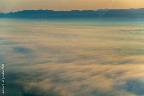 Aerial view of the valley in early morning mist  beautiful in the highlands. Low clouds and fog cover the sleeping meadow. Alpine mountain valley mists landscape at dawn. Serene moment in rural area