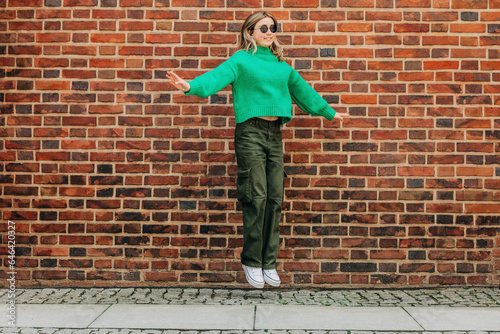 Teenage girl jumping in front of brick wall photo