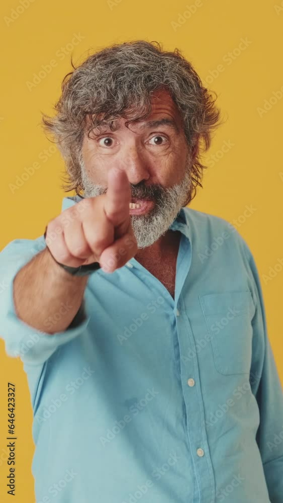 Elderly gray-haired man points with forefinger and raising thumb up, isolated on orange background Elderly gray-haired man points with forefinger and raising thumb up, isolated on orange background