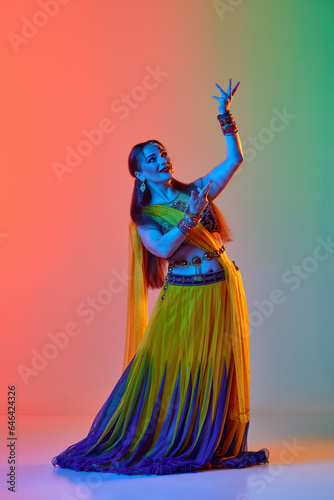 Odissi dance. Beautiful woman in indian costume, with makeup and accessories dancing against gradient studio background in neon. Concept of beauty, fashion, India, traditions, choreography, art. Ad